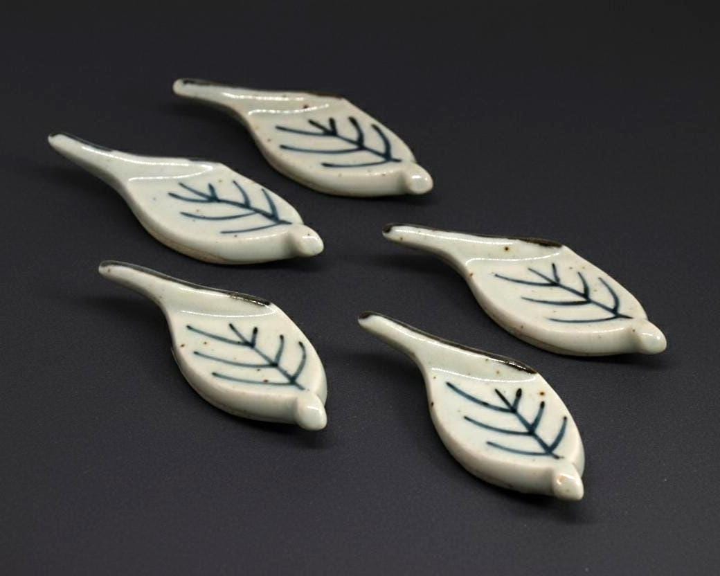 Ceramic leaf chopstick rests set showing front design on a dark surface.