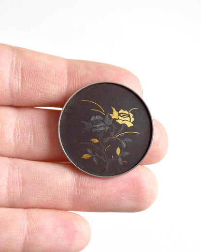 Amita Black Gold Damascene Floral Brooch held next to a hand to demonstrate scale
