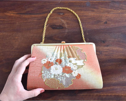 Floral Woven Kimono Clutch held next to a hand on a wooden surface for scale