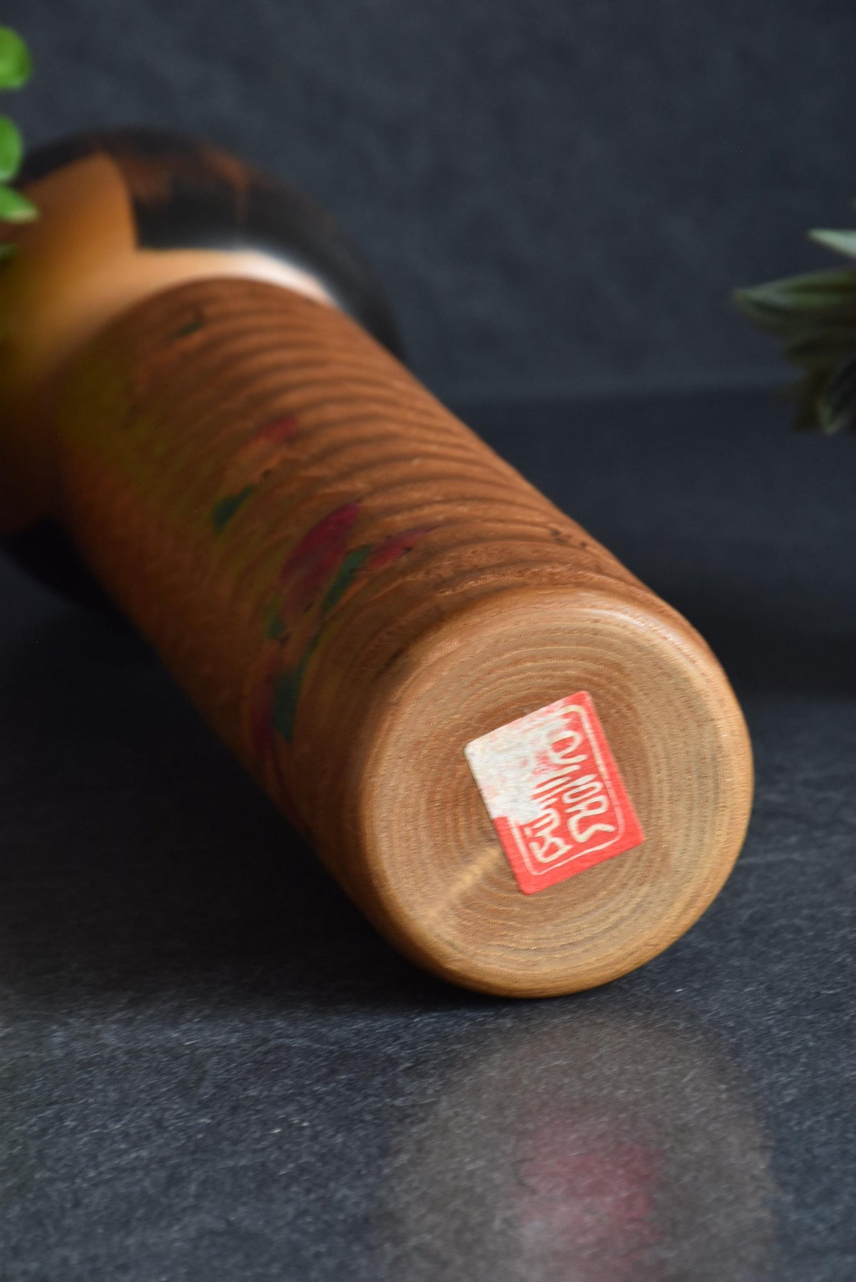 Usaburo Sosaku Kokeshi doll base showing the bottom with a partially peeled maker mark sticker
