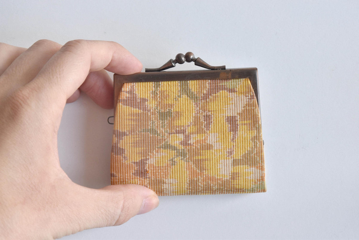 Oshima Tsumugi Silk Gamaguchi Coin Purse held next to a hand to demonstrate its compact size and scale