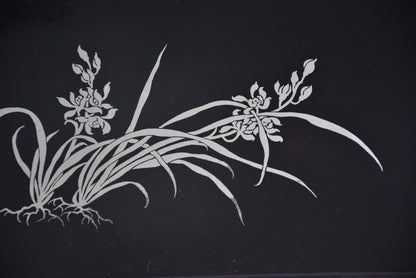 Close-up angle highlighting the detailed silver orchid flower and root pattern on the tray