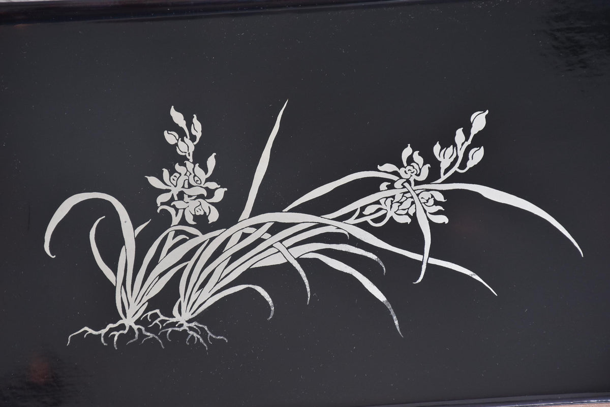 Close-up of the silver orchid inlay design featuring flowing leaves and roots on the tray