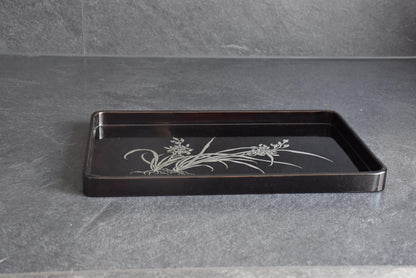 Black lacquer serving tray shown from a low angle resting on a dark slate countertop surface