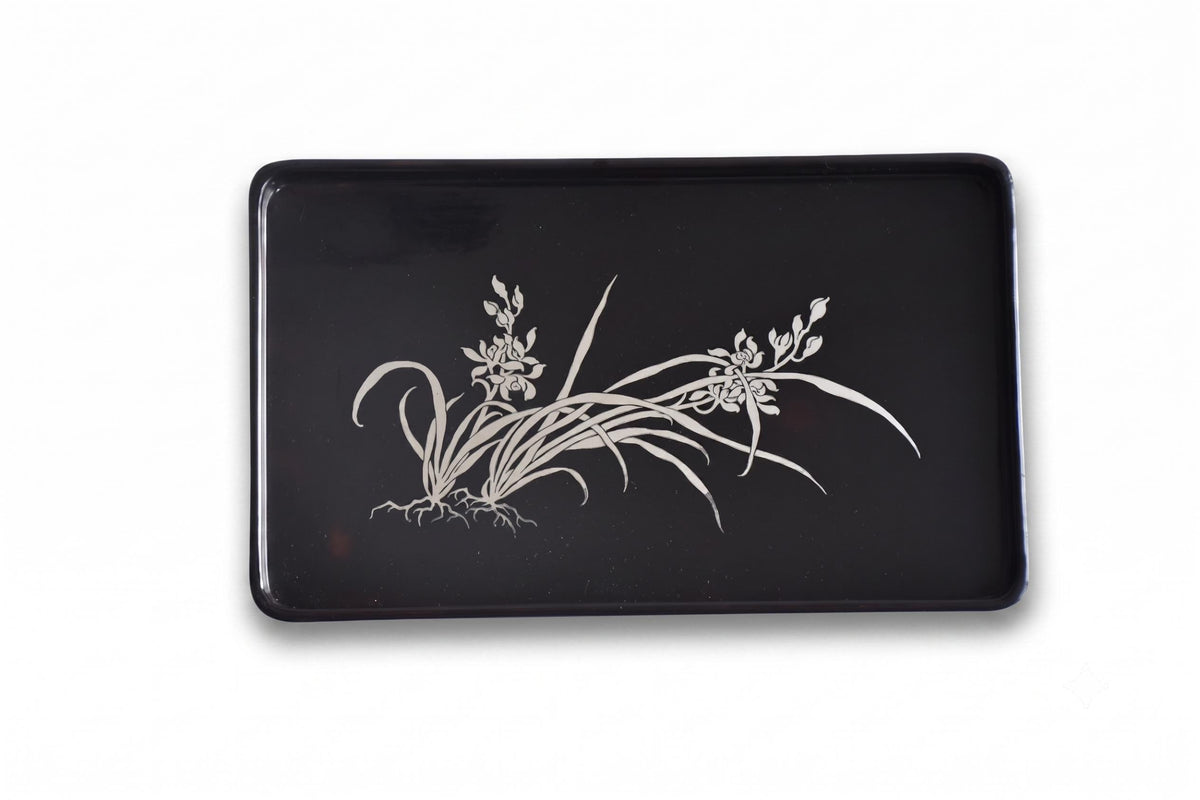 Black lacquer serving tray with silver orchid inlay viewed from above against a white background