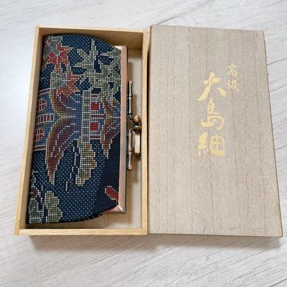 Blue Oshima Tsumugi Silk Gamaguchi Coin Purse positioned alongside its wooden storage box lid