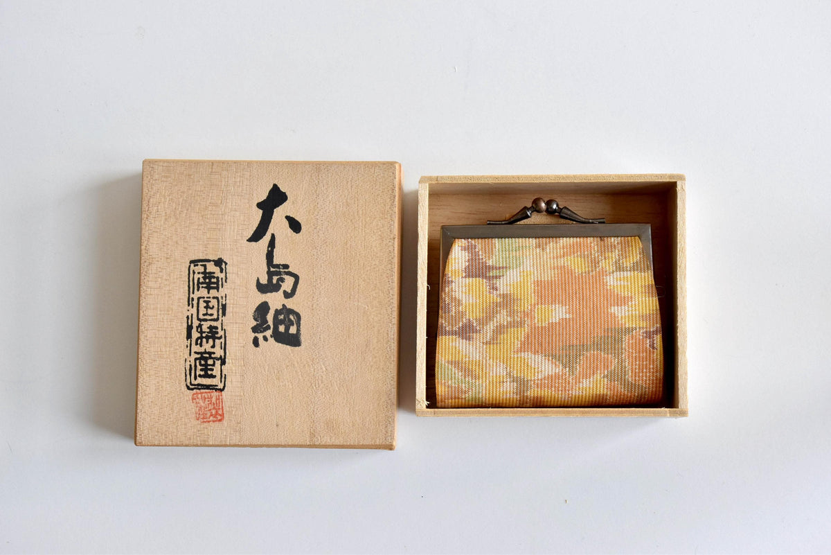 Oshima Tsumugi Silk Gamaguchi Coin Purse resting inside its open wooden storage box with calligraphic lid