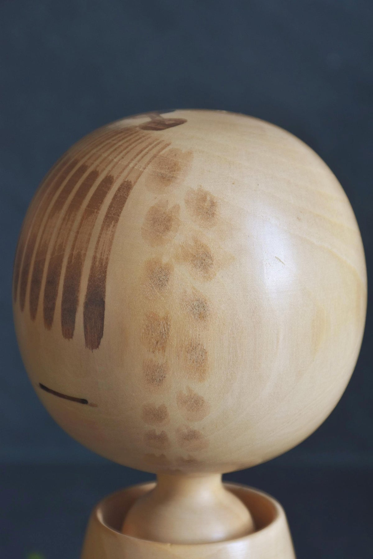 Chiyomatsu Kano kokeshi head close-up showing painted bangs and single-stroke closed eyes on the rounded face