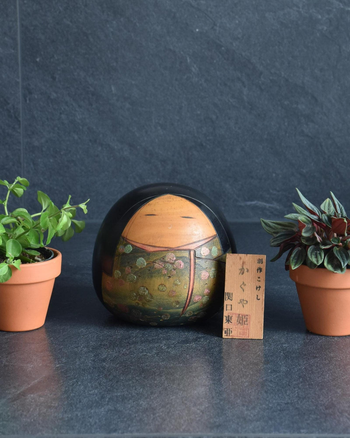 Toa Sekiguchi Kaguya Hime Sosaku Kokeshi Doll resting between two small potted plants
