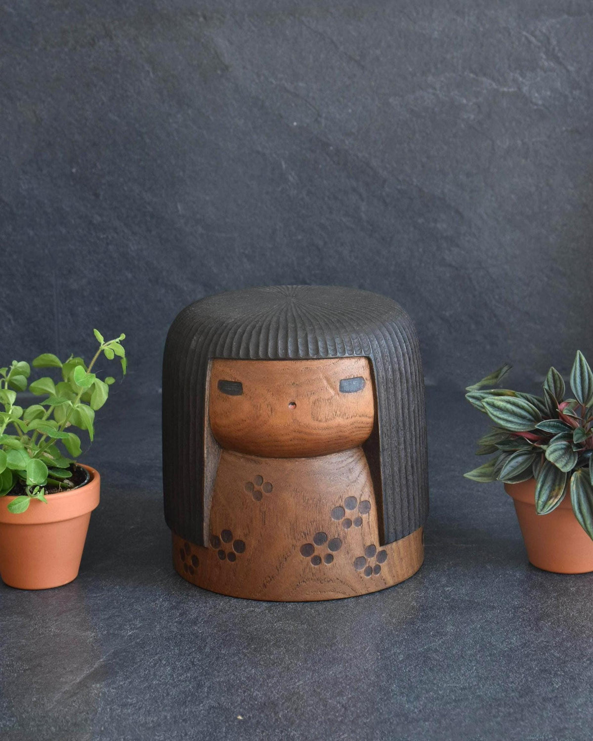 Sanpei Yamanaka Sosaku Kokeshi Harunone Wood Doll displayed between small potted plants