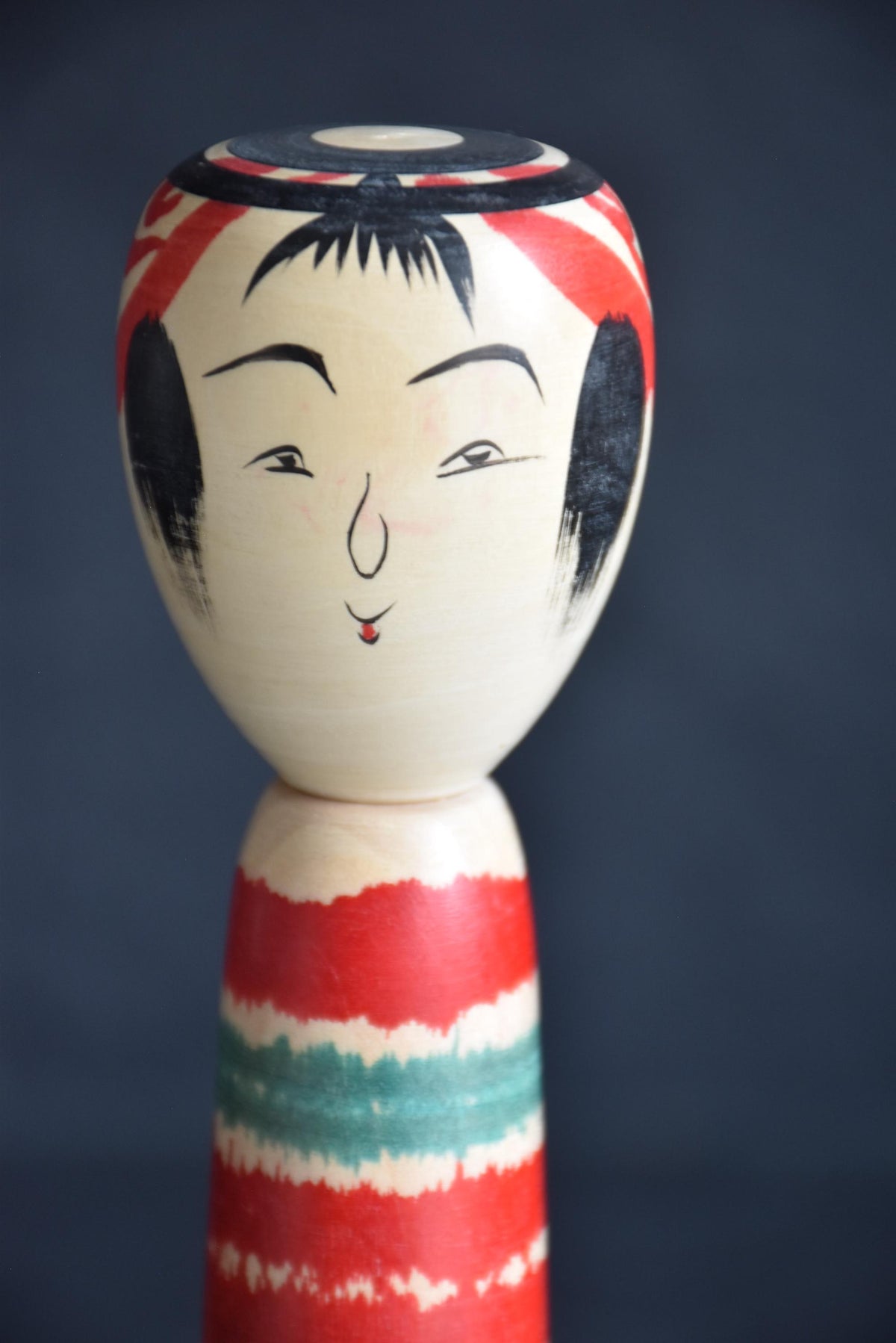 Tsuchiyu-Kei kokeshi head close-up showing painted facial features and red hair decoration