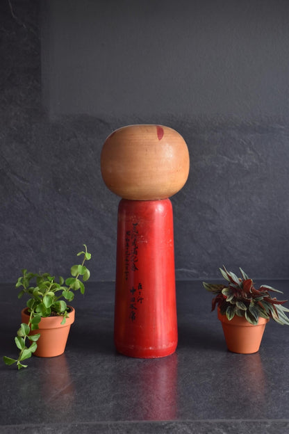 Hakuho Sosaku Kokeshi doll back view showing Japanese black calligraphy text painted vertically on the red-lacquered body.