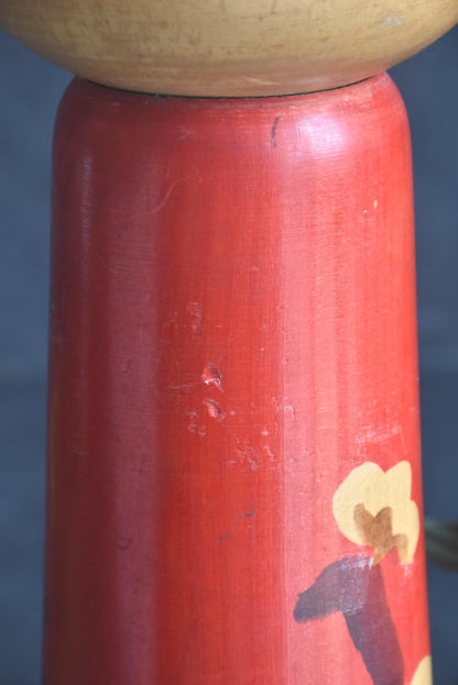 Hakuho Sosaku Kokeshi doll wear detail showing small scratches and signs of aging on the red-lacquered wooden body.