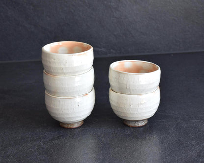 Set Of 5 White Kumidashi Teacups arranged in two small stacks on a dark surface next to the storage box