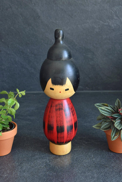 Hideo Ishihara Sosaku Kokeshi Doll Yukake Red Sunset standing between potted plants
