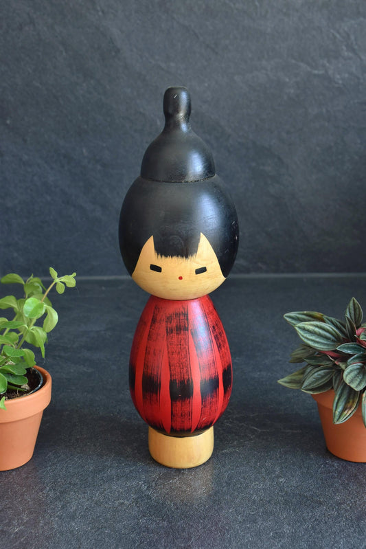 Hideo Ishihara Sosaku Kokeshi Doll Yukake Red Sunset standing between potted plants