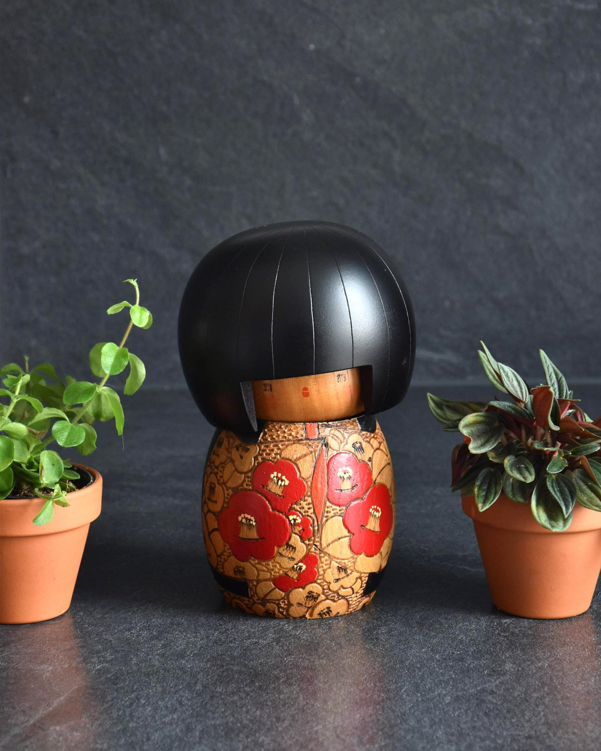 Kazuo Takamizawa kokeshi doll viewed from the front between two potted plants