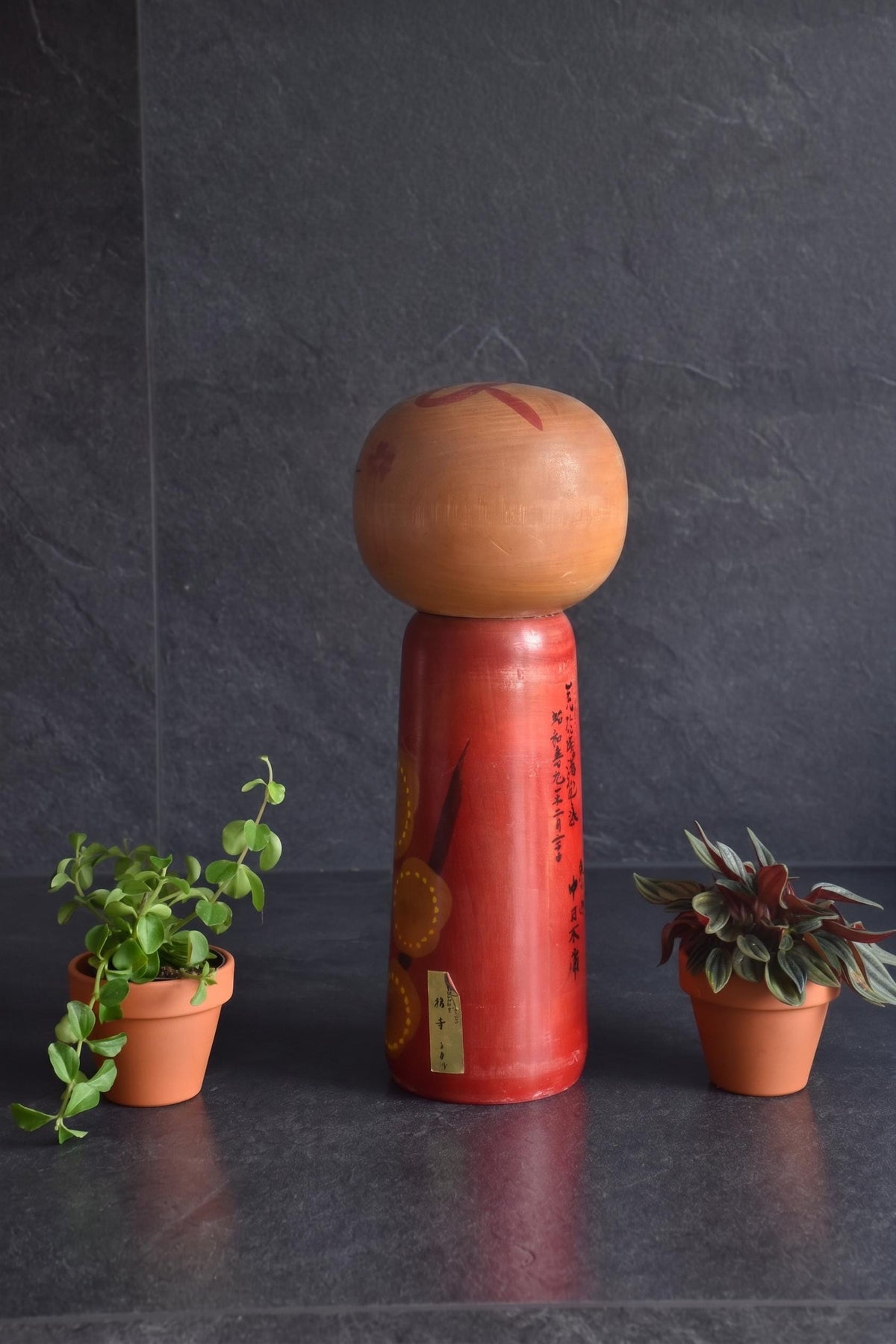 Hakuho Sosaku Kokeshi doll angled back view showing both Japanese text and a small gold maker sticker on the red body.