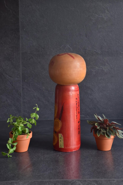 Hakuho Sosaku Kokeshi doll angled back view showing both Japanese text and a small gold maker sticker on the red body.