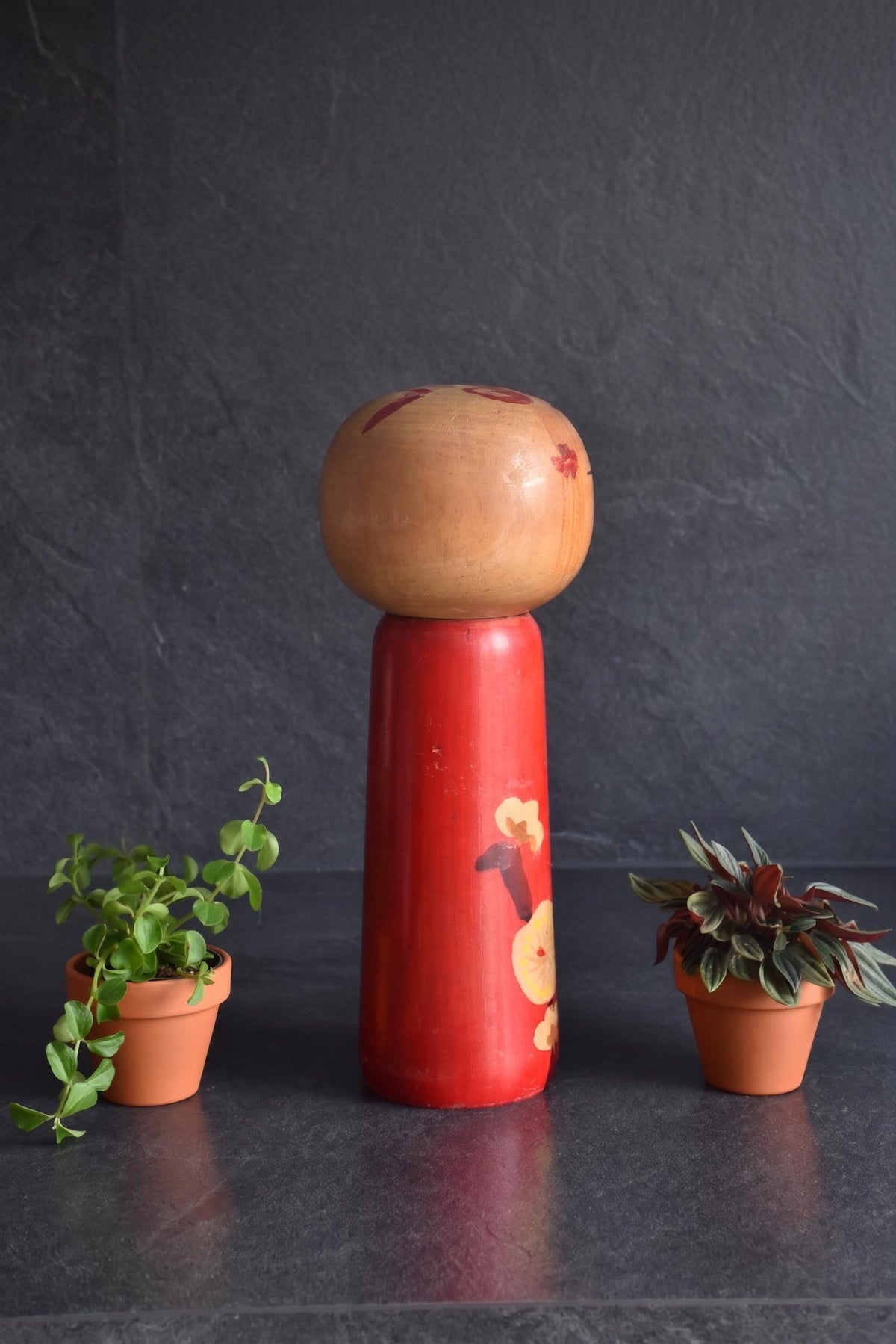 Hakuho Sosaku Kokeshi doll three-quarter view showing the face, hair ornaments, and side of the red plum blossom body.