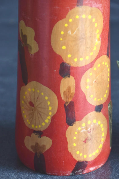 Hakuho Sosaku Kokeshi doll pattern detail showing close up of hand-painted yellow blooming plum blossoms on red lacquer.