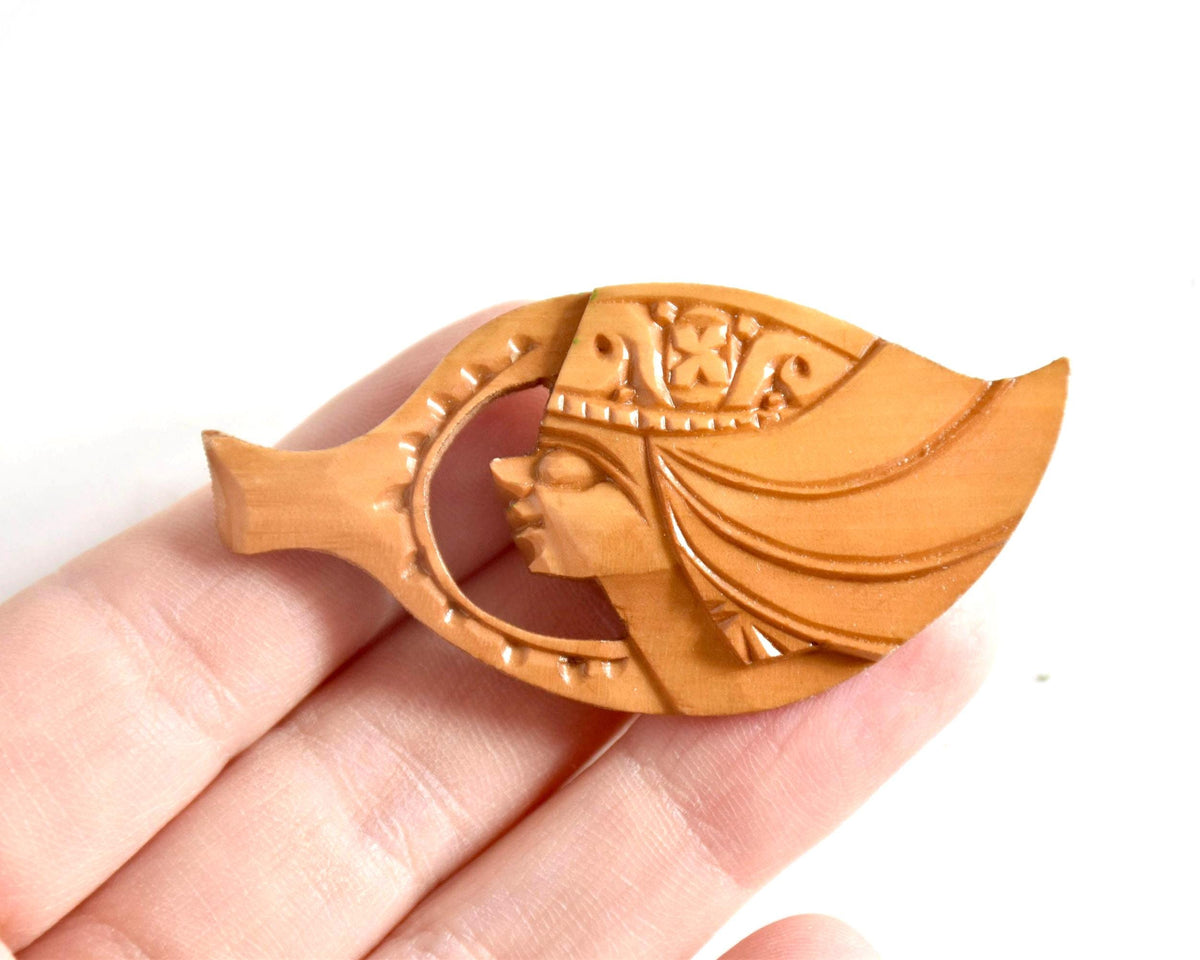 Ainu hand-carved wooden brooch showing scale next to a hand