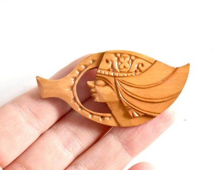 Ainu hand-carved wooden brooch showing scale next to a hand