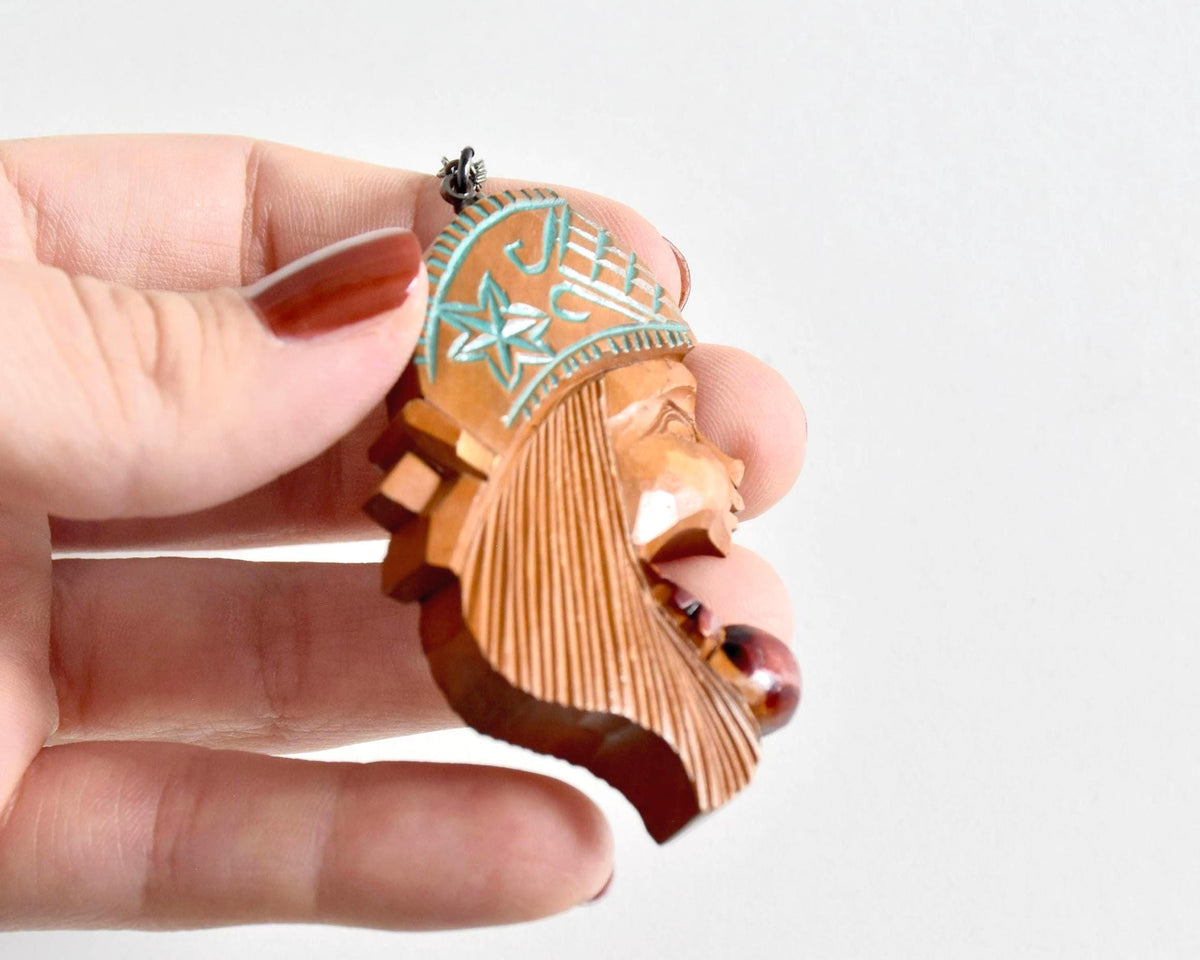 Ainu double-sided wooden pendant necklace held by fingers showcasing the thickness and carved profile relief