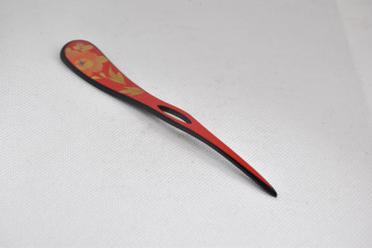 Red lacquered kanzashi hair accessory angled view showing the decorated paddle