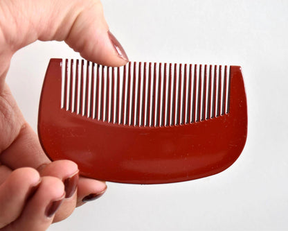 Toyama Urushi Kushi comb backside held in a hand showing minor scratches on the red lacquer