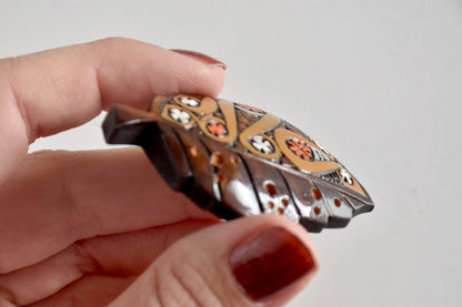 Side profile of Ainu leaf brooch held in hand showing wood thickness