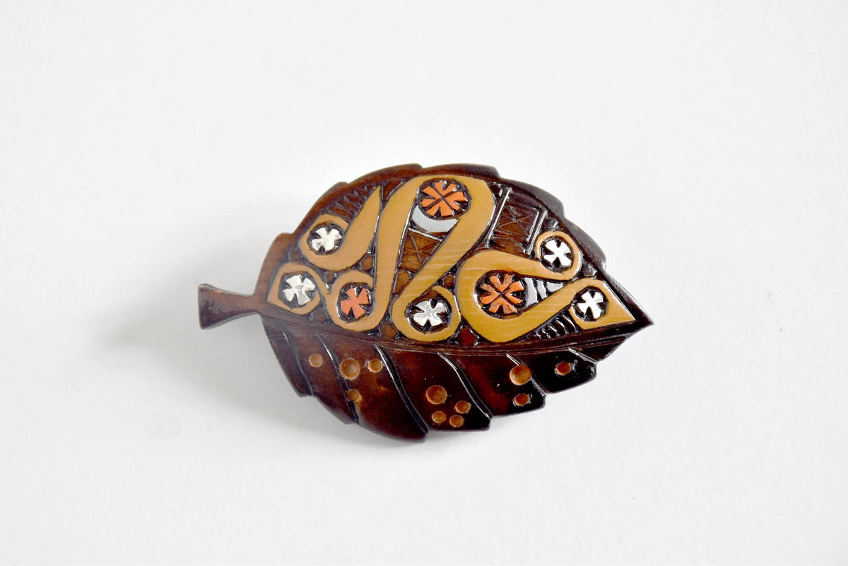 Ainu leaf brooch displaying intricate carved moreu patterns on white