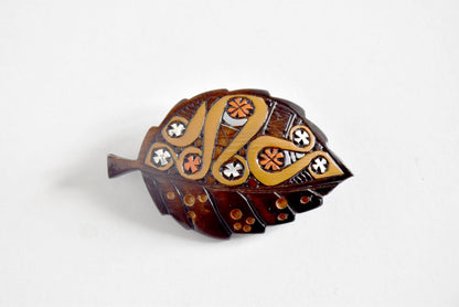 Ainu leaf brooch displaying intricate carved moreu patterns on white