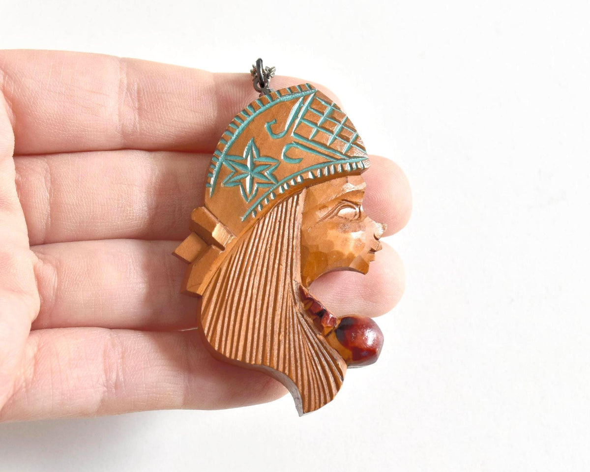 Ainu double-sided wooden pendant necklace held in hand to demonstrate the scale and hand-carved texture