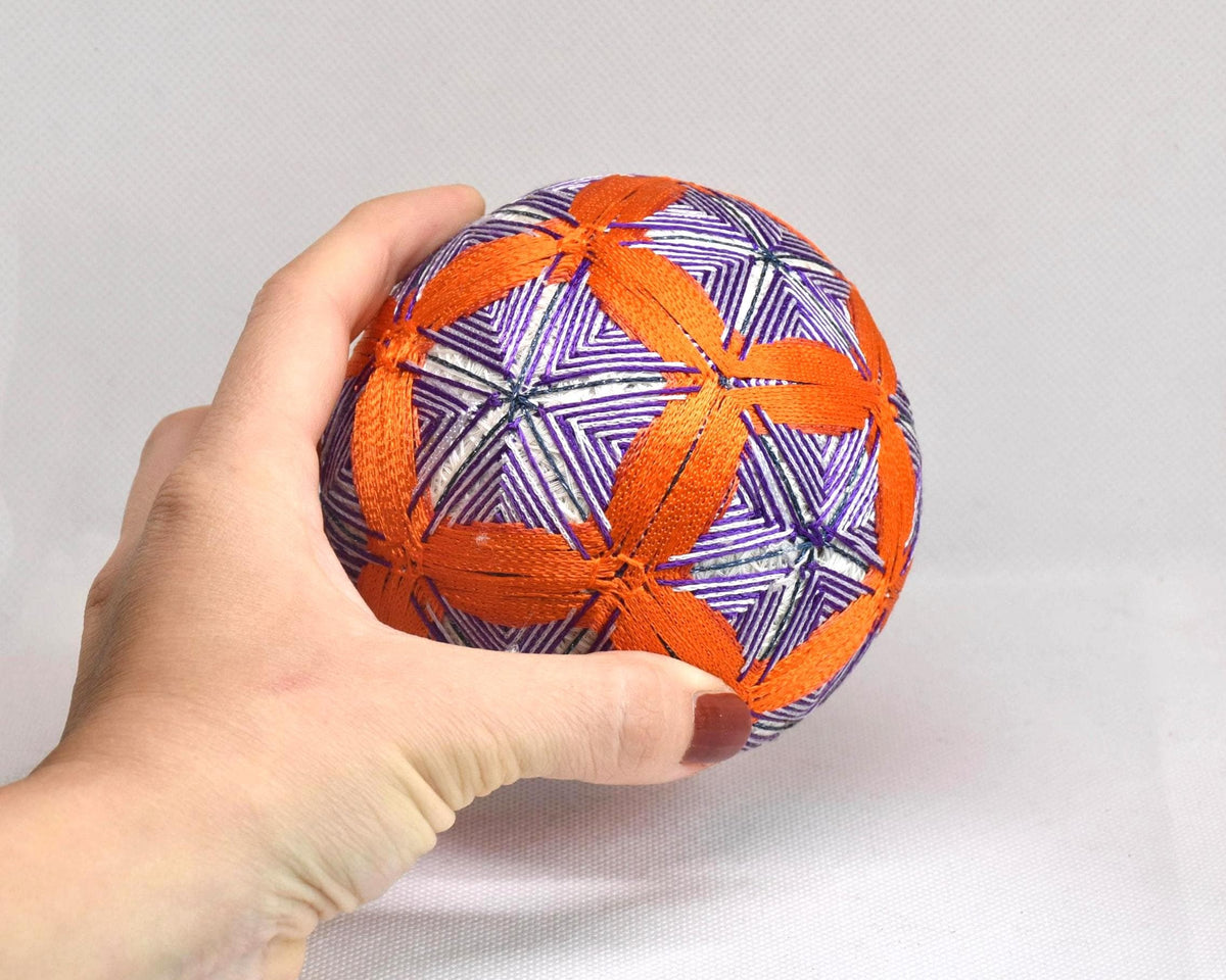 Hand-Embroidered Temari Ball Orange And Purple table scatter held next to a hand for size comparison