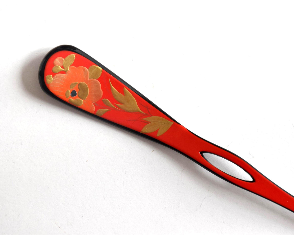 Red lacquered kanzashi hair accessory showing the floral maki-e paddle detail