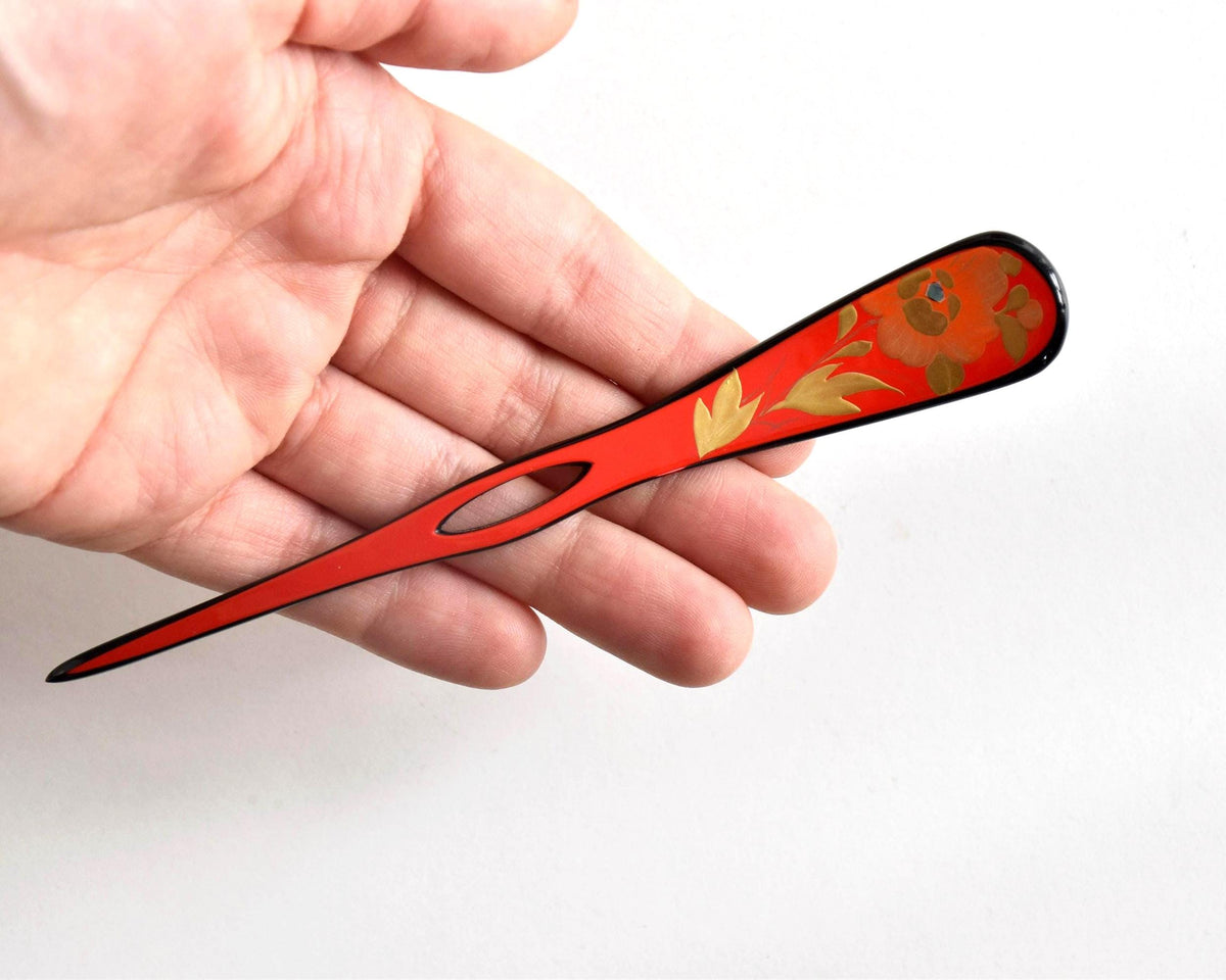 Red lacquered kanzashi hair accessory held in a hand for scale