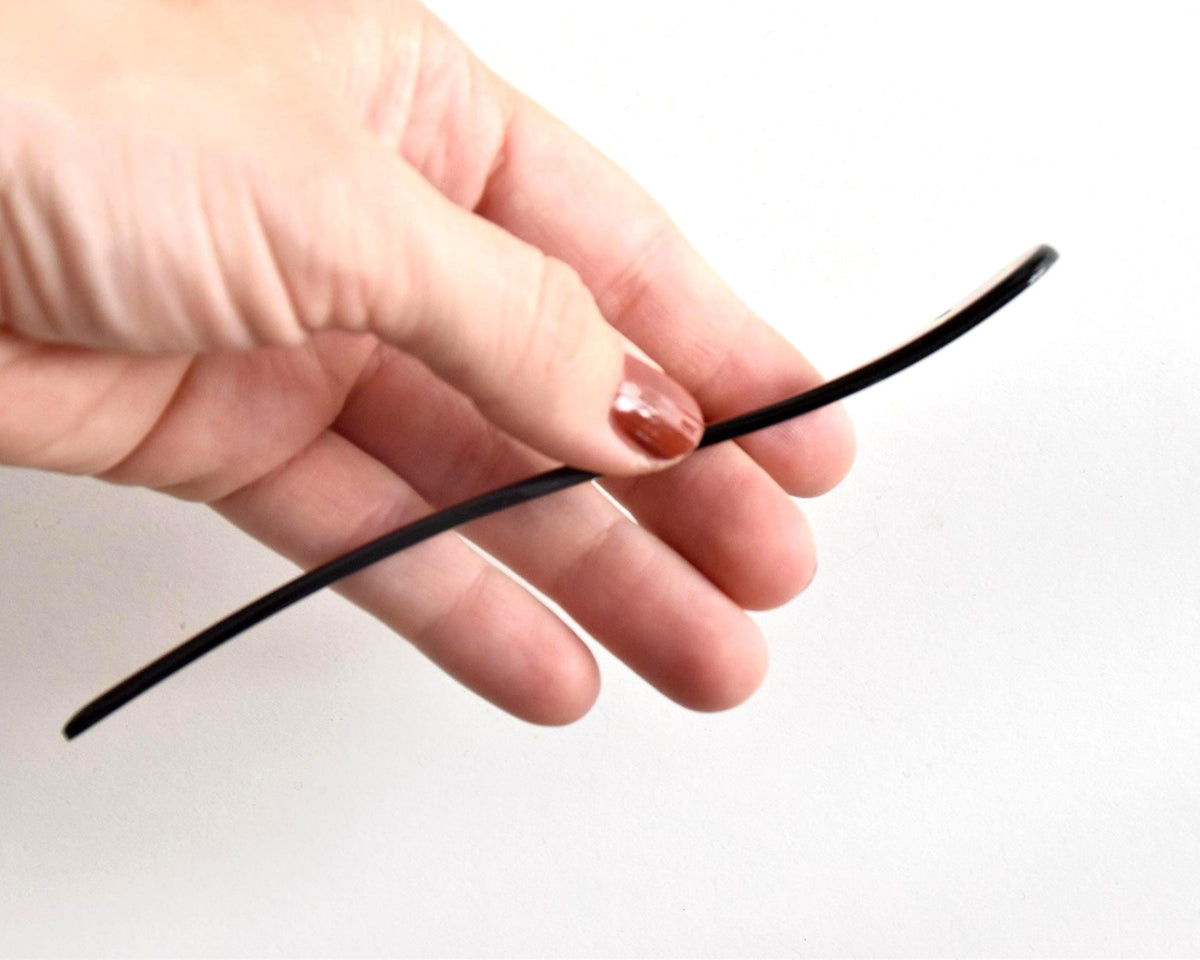 Red lacquered kanzashi hair accessory shown in profile curved shape held in hand
