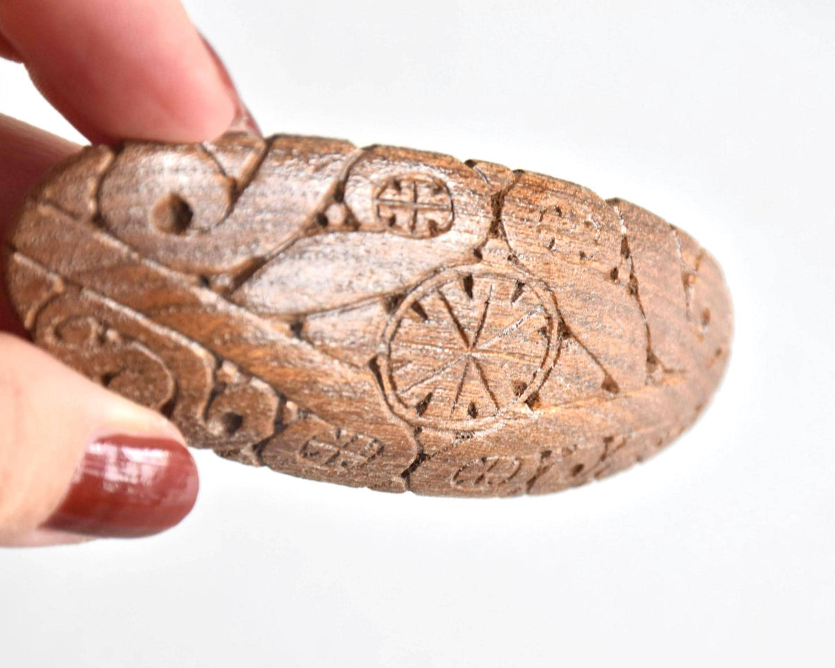 Ainu wooden hair barrette shown next to a hand to display its size and carved surface texture