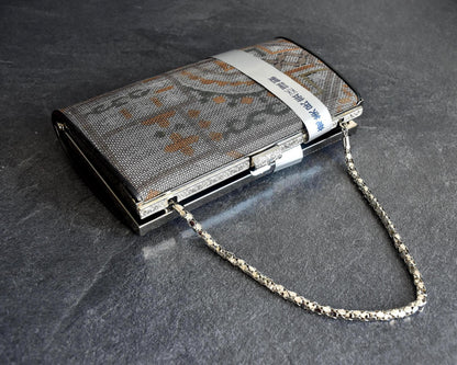 Amami Oshima Tsumugi silk clutch angled view showing metallic chain strap