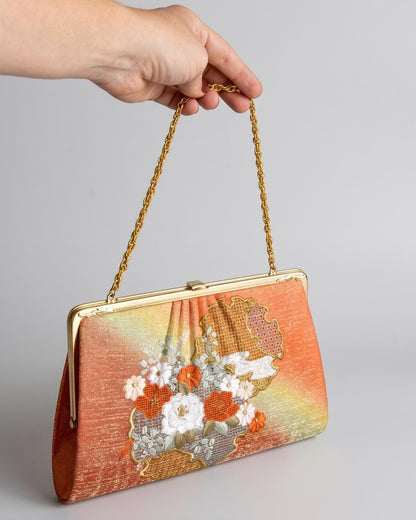 Floral Woven Kimono Clutch With Ornate Metal Frame held up by a hand with a metal chain attached
