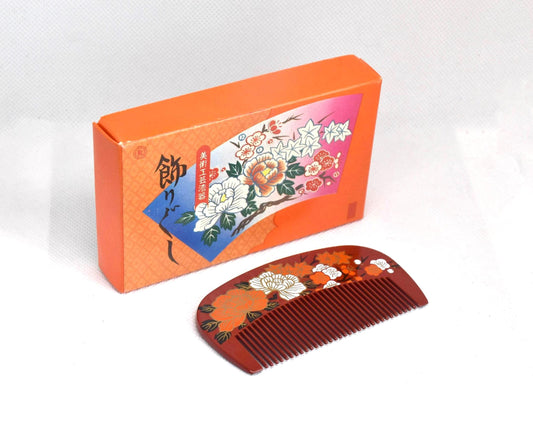Toyama Urushi Kushi Comb With Peony And Plum Motif next to its original orange presentation box