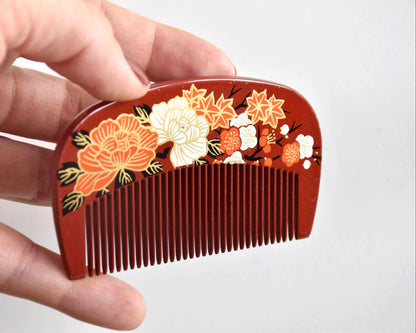 Toyama Urushi Kushi comb held next to a hand to show its actual size of 8.9 cm by 5 cm