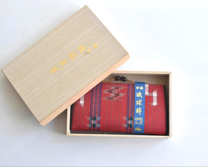 Ryukyu Kasuri Geometric Ikat Silk Wallet Red displayed alongside the wooden box top