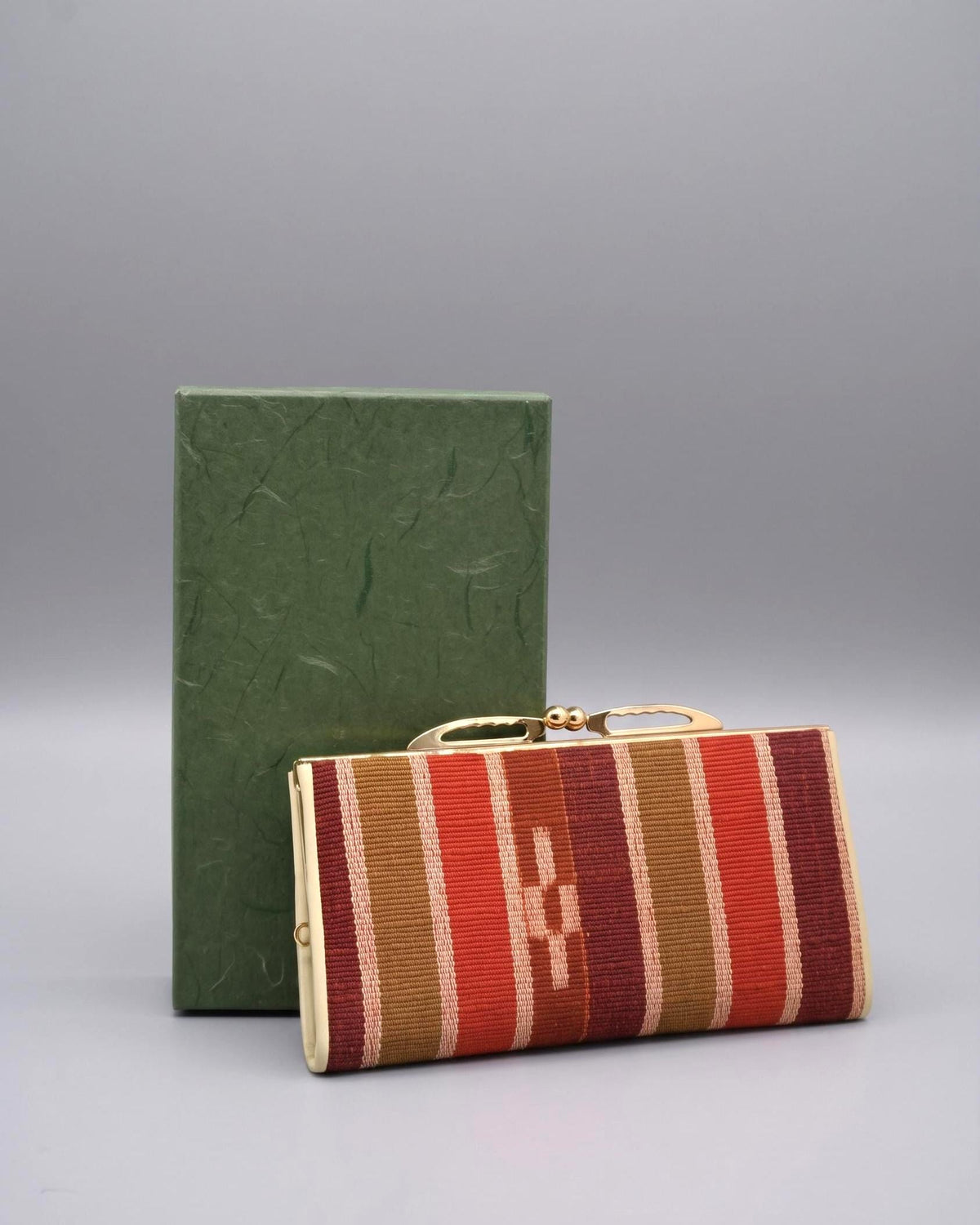 Yaeyama Minsa-Ori Red Kasuri Clasp Coin Purse with its green original storage box on a grey surface