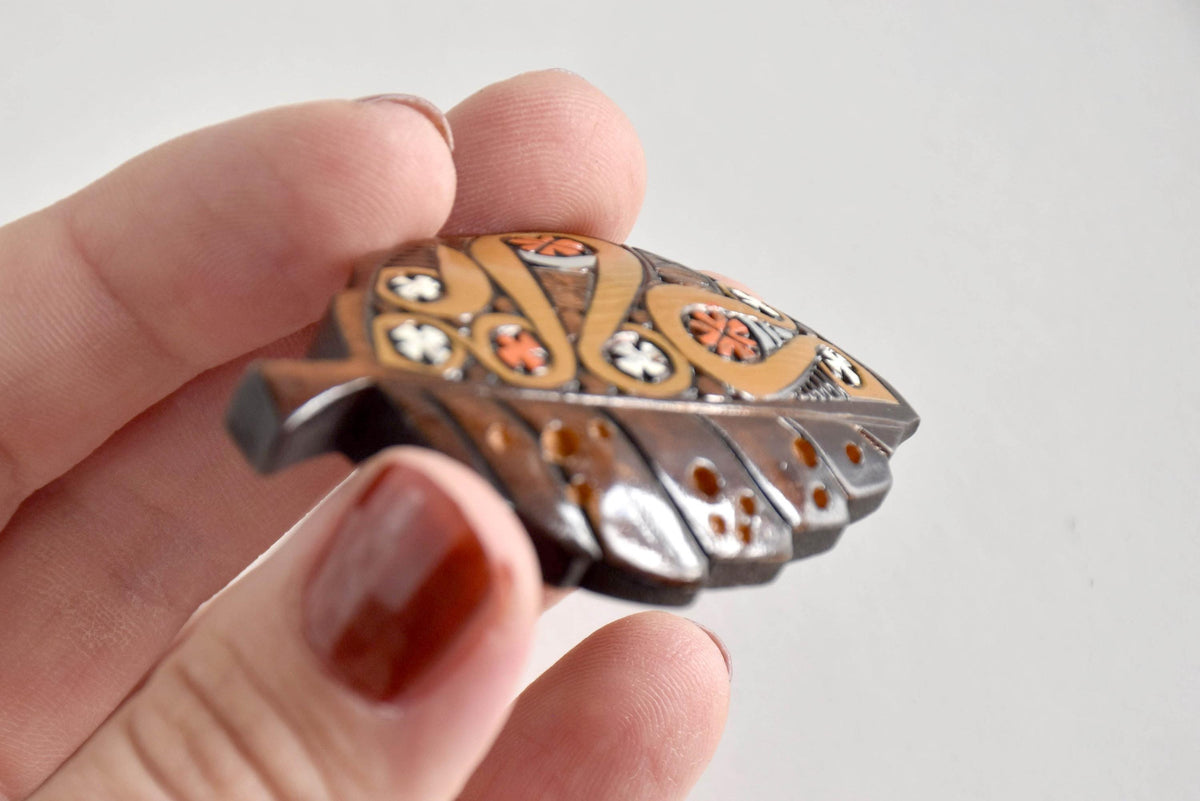 Side view of Ainu leaf brooch held in hand highlighting polished surface
