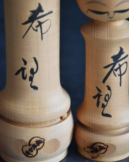 Isamu Ise kokeshi dolls featuring inscribed hope kanji and stamped rim details.