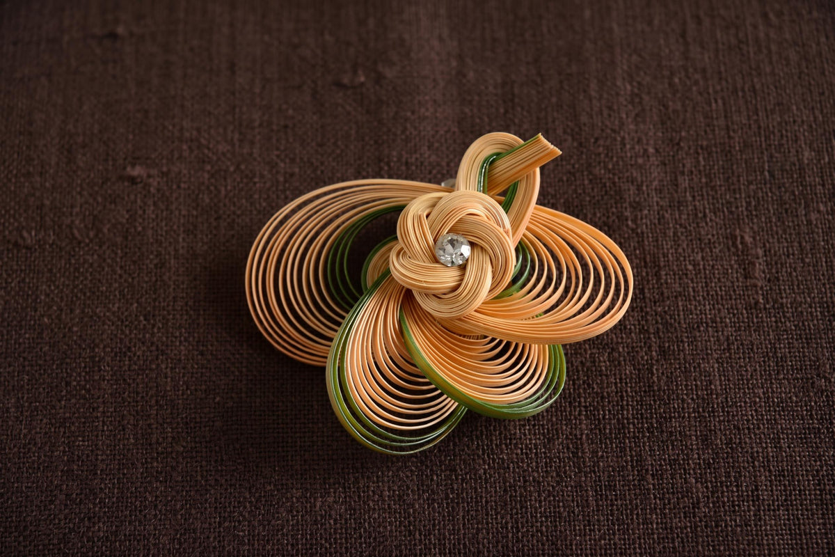 Hand-Woven Bamboo Knot Brooch In Beige And Green placed on brown fabric