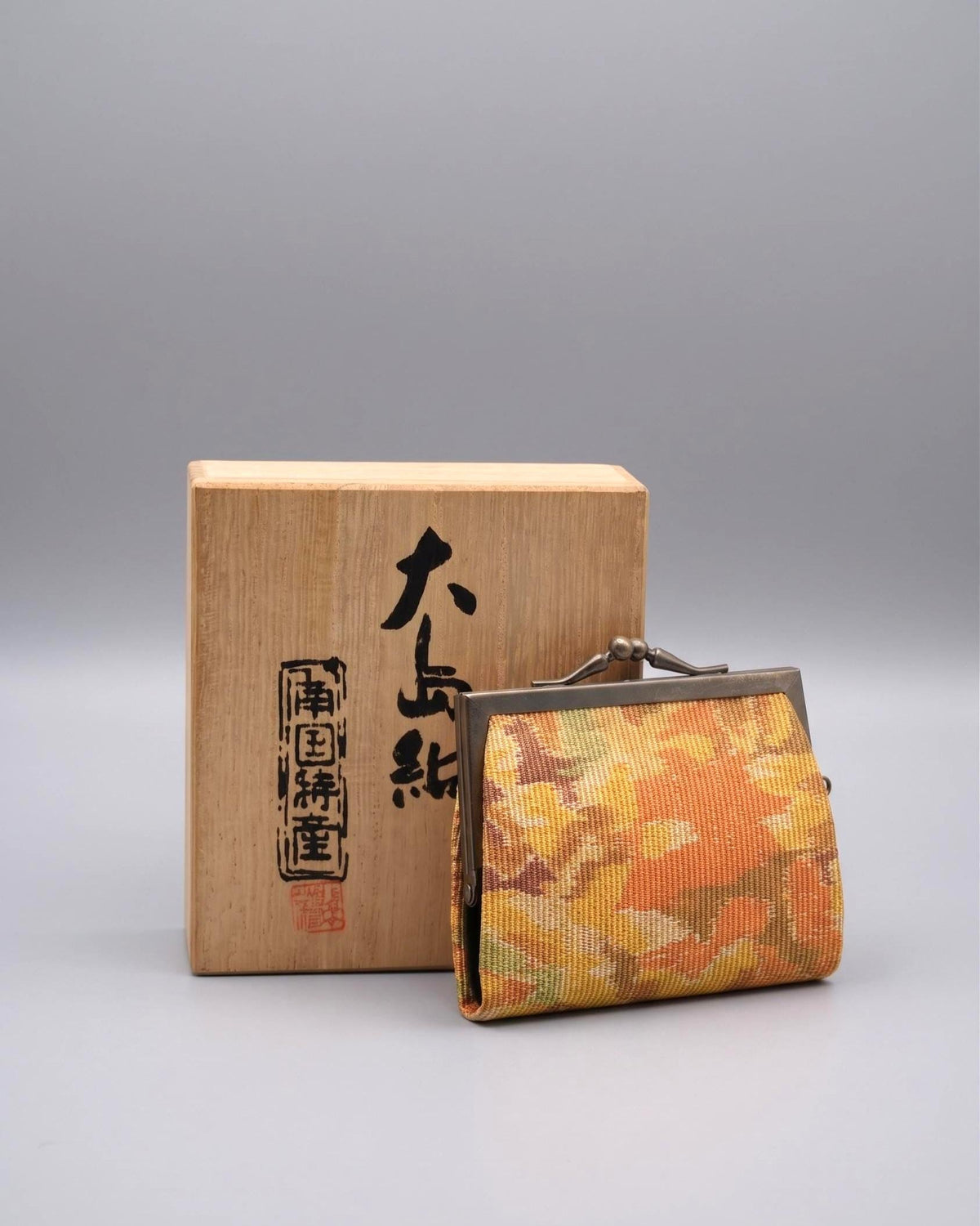 Oshima Tsumugi Silk Gamaguchi Coin Purse with mud-dyed fabric and traditional metal clasp next to its box