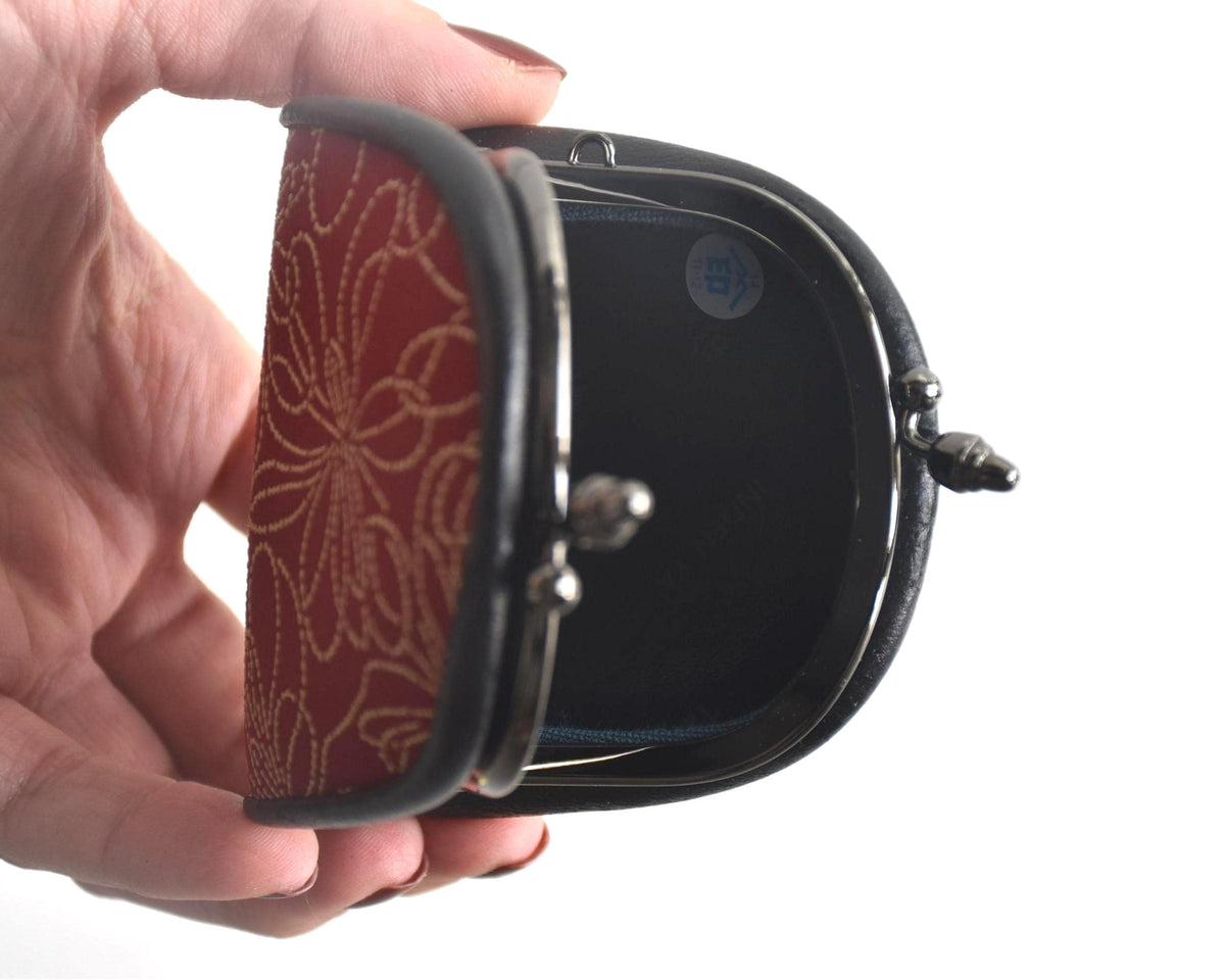 Inden deerskin coin purse held in hand showing the opened interior and metal clasp mechanism